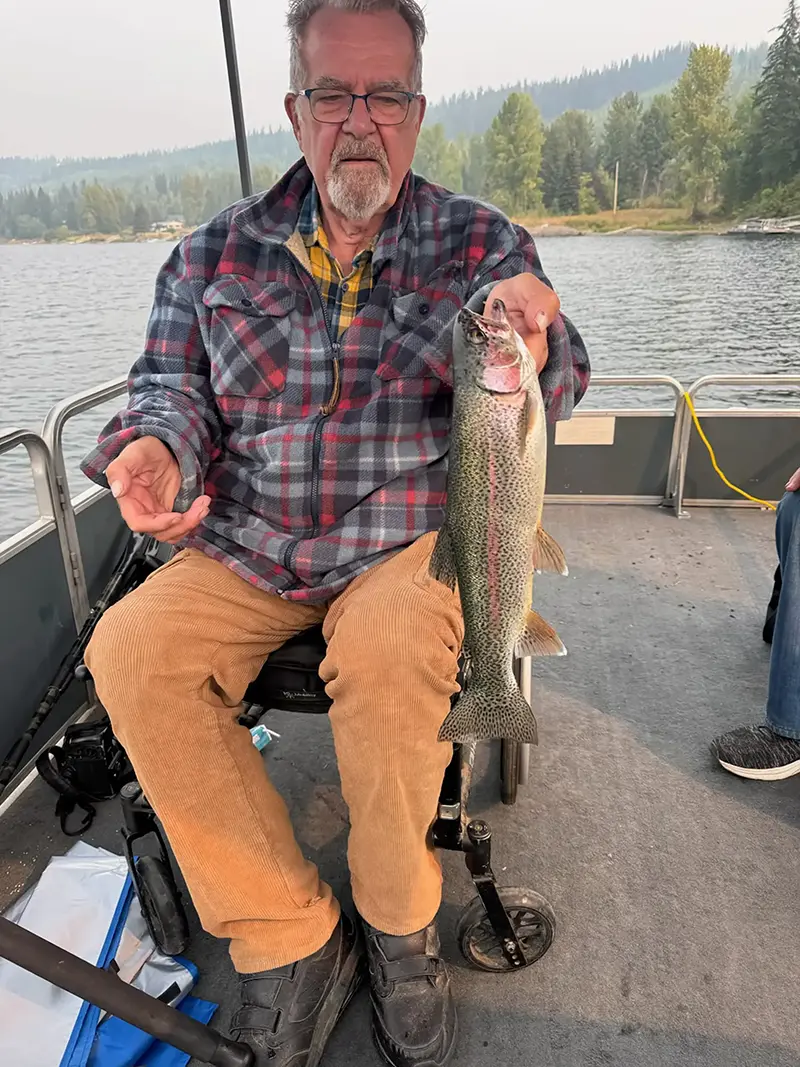 A smiling guest in a wheelchair aboard our pontoon boat, holding a large wild rainbow trout